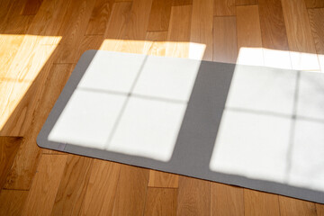 High angle view of the grey foam yoga or pilates mat laying on natural wooden floor during the sunny day. Sport and recreation concept