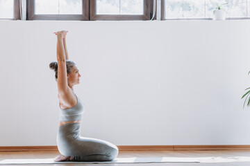 Side view of the still yoga senior woman meditating with hands up at home in morning. Healthy...