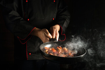 The chef prepares food in a frying pan with steam. The concept of restaurant and hotel service