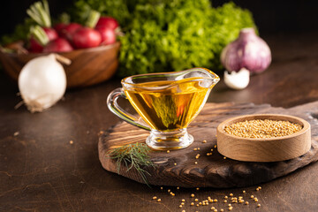 Mustard oil on wooden board background with fresh vegetables. Copy space