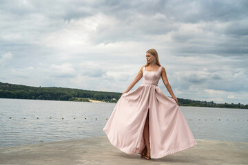 Fototapeta na wymiar Young woman enjoying summer time posing alone in cute ping dress near lake