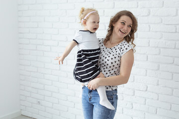 Mother holds and having fun child with hearing aids and cochlear implants on white brick wall with copy space . Deaf and diversity and innovating medicine technologies concept