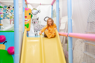 a happy little girl slides down the slide into the dry pool with plastic balls.