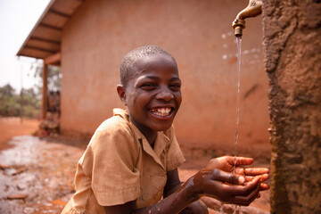 Smiling black african schoolboy drinking from a tap outside during recreation - obrazy, fototapety, plakaty