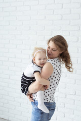 Mother holds her child with hearing aids and cochlear implants on white brick wall . Deaf and diversity and health concept