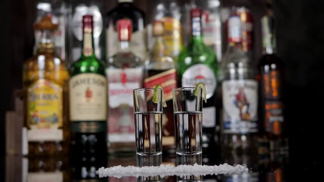Close-up of a man and a woman taking shots of tequila with lime and salt in a bar. A couple drinks in a nightclub or bar against the background of shelves with bottles of alcohol.