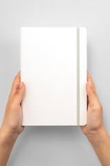 Female hands holding white book with blank cover on grey background, top view