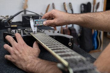 Fototapeta na wymiar Latin American luthier calibrates the strings of an electric guitar with a digital vernier. Unrecognizable. Guitar concept, calibration, instrument.