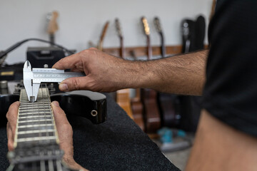 Latin American luthier accurately calibrates the strings of an electric guitar with a vernier. person Unrecognizable. Guitar concept, calibration, instrument.