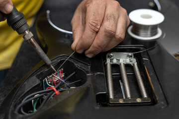 Latin American luthier's hands soldering with a soldering iron and tin the wires of the microphone...