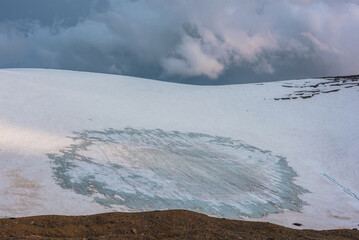 Dramatic landscape with glacier on sunlit high snow mountain under cloudy sky at sunset. Beautiful alpine landscape with large snowy mountain in sunlight under evening clouds at changeable weather.