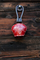 Traditional swiss cow bell red and white, decorative souvenir on wooden background, vertical