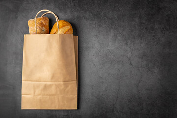 Disposable paper bag from a supermarket recyclable with whole baked loaves of bread flatlay on dark...