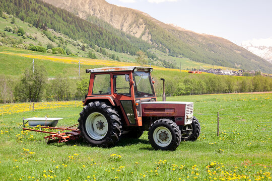 Tractor in alpine village on a green meadow, mountains on the background