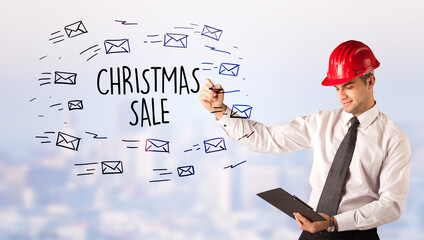 Young businessman with helmet drawing sale sign