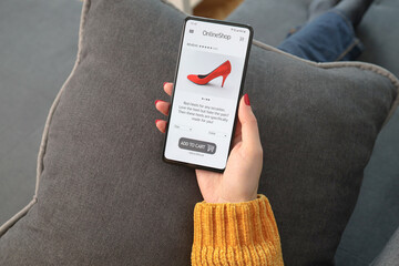 Female hand holding mobile phone with open page of online shoe store on screen. Woman shopping...