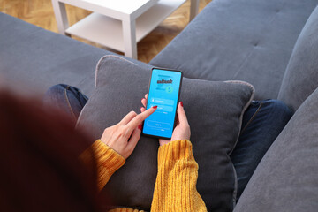Woman checking balance on her online bank account via smartphone. Female hand using mobile banking while relaxing on sofa.