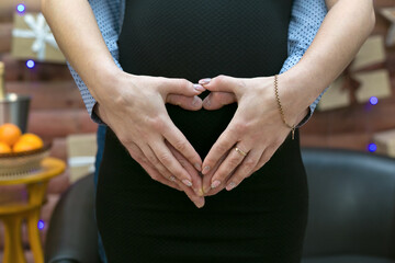 The fingers of male and female hands are folded form of a heart on the stomach of a pregnant woman.