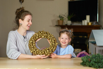 Christmas wreath of golden walnuts. woman and child smile close up. Make own golden nut for Cinderella. babysitter play with child. Mom and daughter together at home table. How to make wreath. DIY.