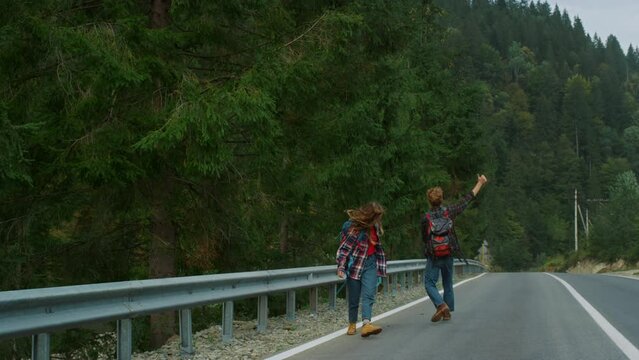 Dancing lovers walk hitchhike on forest roadside. Couple hikers jump in mountain