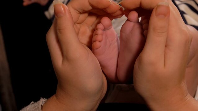 Hands of an adult are forming a heart gesture with little adorable babys feet