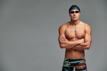 Obraz premium Portrait of a swimmer in a cap and mask, half-length portrait, young athlete swimmer wearing a cap and mask for swimming, copies of space, gray background.