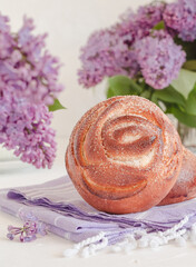 Fresh delicious cinnamon bun on a table with lilac flowers. Kanelbullar - swedish cinnamon rolls, swirl.