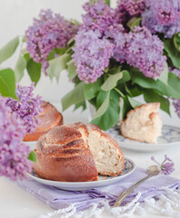 Sliced cinnamon bun on a plate on a table with lilac flowers. Kanelbullar - swedish cinnamon rolls.