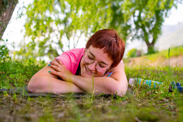 Naklejka na ściany i meble Beautiful young woman smiling and dreaming while lying on the floor after working out on warm summer day