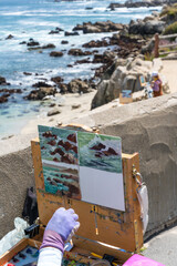 Dramatic image of art lessons wi5h a artist canvas and a easel with hand painting the Monterey coast in California, with the waves and rocks and sandy beach in background, 