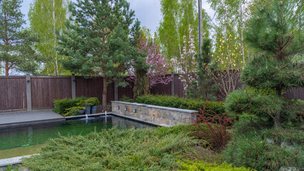 Pond in landscape design. Landscape design on backyard. View of small pond, trimmed bushes and small fountain.
