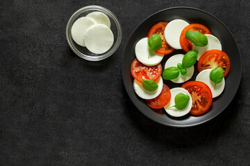 Caprese, Italian appetizer of mozzarella, basil and tomatoes, on gray plate, on dark background, top view, space to copy text.