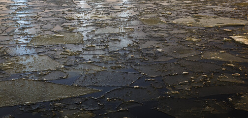 Background image, pieces of ice in the river at night in a lighted area, reflection of light.