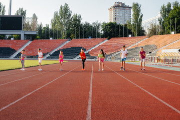 Naklejka premium A large group of children, boys and girls, run and play sports at the stadium during sunset. A healthy lifestyle.