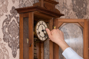 A man winds up an old wall clock with a key.
