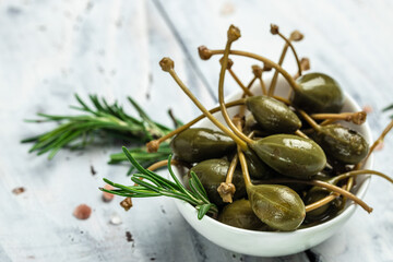 Capers. Marinated or pickled canned capers fruit with fresh rosemary in a small bowl, on gray background. place for text, top view