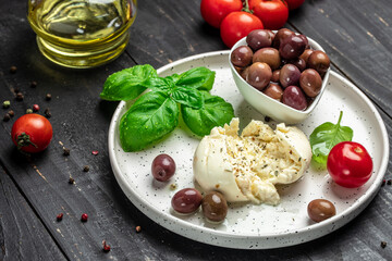 Creamy Italian Burrata Cheese with basil, olive oil and cherry tomatoes on white plate on dark wooden background. banner, menu, recipe place for text, top view