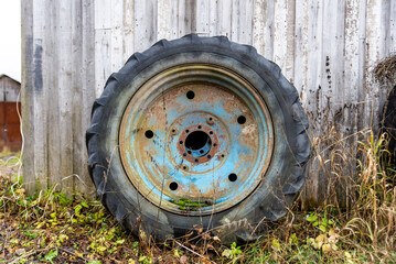 a large blue rusty wheel from a tractor stands near the wall of the barn
