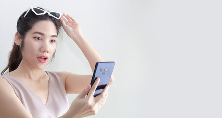 Naklejka premium Asian beautiful woman looking on smartphone and raise hand touch on sun glasses and open mouth with surprising during chatting or shopping online or win lottery or win game