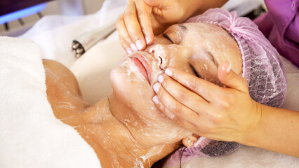 Cosmetologist applies  a moisturizing mask on female face. Woman in a spa salon on cosmetic...