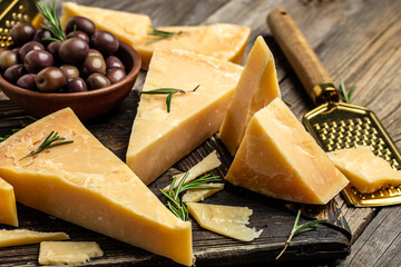 Parmesan cheese on a wooden board, Hard cheese, olives, rosemary and metal grater. place for text, top view