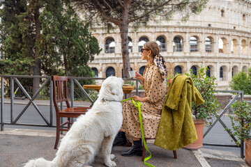 Woman sitting with her dog at outdoor cafe near coliseum, the most famous landmark in Rome. Concept of italian lifestyle with pets and traveling Italy - obrazy, fototapety, plakaty