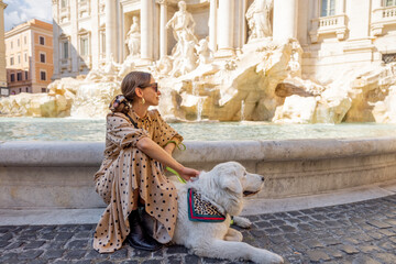 Woman sitting with dog on famous di Trevi fountain in Rome. Woman traveling with her white huge...