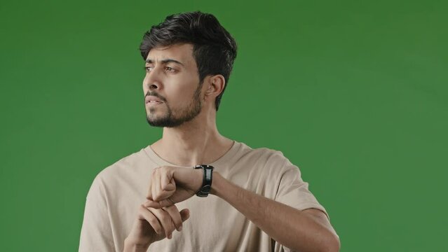 Portrait of serious impatient arabian man guy waiting for meeting over green background looking at clock frustrated hispanic guy businessman checking time on wrist watch annoyance being late lateness