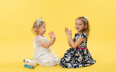 Little girls play, sit on the floor in the studio. Yellow background