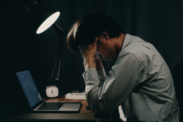young japanese man holding head due to stress and tiredness at desk