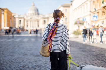 Stylish woman walks with a dog on the street on background of saint Peter's cathedral in Rome. Concept of italian lifestyle and travel - obrazy, fototapety, plakaty