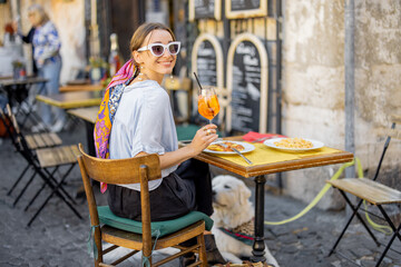 Woman eating italian pasta and drinking wine at restaurant on the street in Rome. Concept of Italian gastronomy and travel. Stylish woman with sunglasses and colorful hair shawl