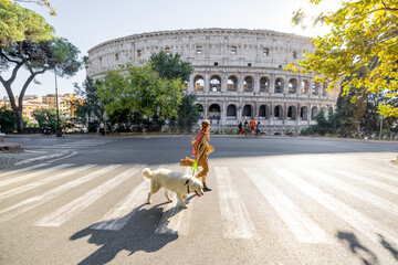 Woman crossing street with her dog in front of Coliseum in Rome. Street view with the most popular...