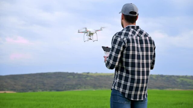 Close up of man farmer in hat standing in green wheat field and controlling a drone which flying above the field. New Technologies in farming. High quality 4k footage